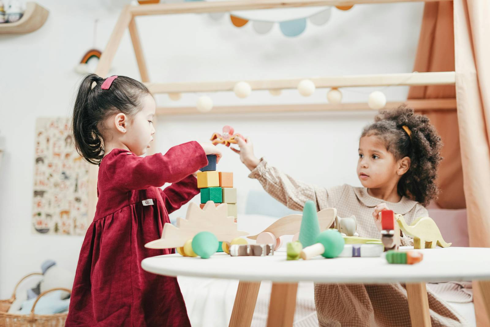 Two young girls playing with wooden toys at a small table